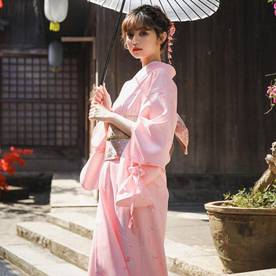 Une femme est vêtue d'un kimono japonais traditionnel et d'un ceinture de geisha Obi autour de la taille. Elle tient dans la main une ombrelle japonaise. La geisha a un Kanzashi dans les cheveux