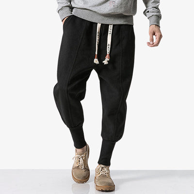 Pour un style streetwear, un homme est habillé avec un pantalon japonais nikka de couleur noir. Le bas du pantalon est cintré. Les cordons sont imprimés avec des kanji japonais