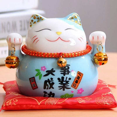 Ce chat maneki neko bleu est en céramique. Cette statuette de chat japonais est posés sur un coussin rouge