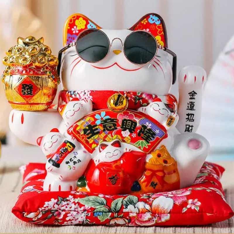 Un grand maneki neko avec une paire de lunette sur le museau. Le chat japonais de la chance a la patte gauche levée pour attirer la bonne fortune