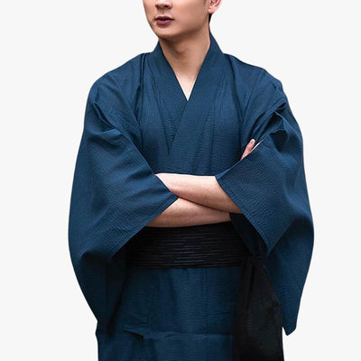 Un japonais est habillé d'un kimono japonais bleubleu foncé pour homme. Ses bras sont croisés sur sa ceinture obi (ceinture de kimono) japonaise noire.
