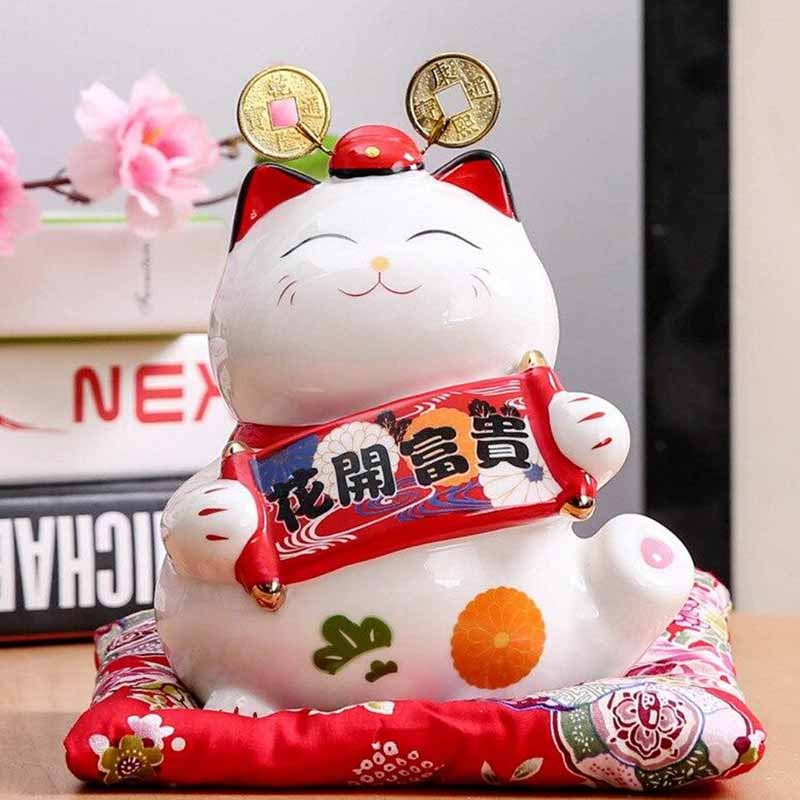 Cette statuette de chat japonais est un maneki neko ruban. Le chat japonais tient dans les pattes un parchemin makemono